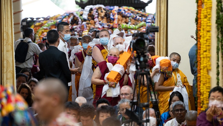 With the large pile of offerings to be distributed to the crowd in the background, members of Foundation for the Preservation of the Mahayana Tradition (FPMT) lined up at the entrance of the Main Tibetan Temple holding offerings to present to His Holiness the Dalai Lama during the Long Life Offering Ceremony in Dharamsala, HP, India on May 24, 2023. Photo by Tenzin Choejor With the large pile of offerings to be distributed to the crowd in the background, members of Foundation for the Preservation of the Mahayana Tradition (FPMT) lined up at the entrance of the Main Tibetan Temple holding offerings to present to His Holiness the Dalai Lama during the Long Life Offering Ceremony in Dharamsala, HP, India on May 24, 2023. Photo by Tenzin Choejor