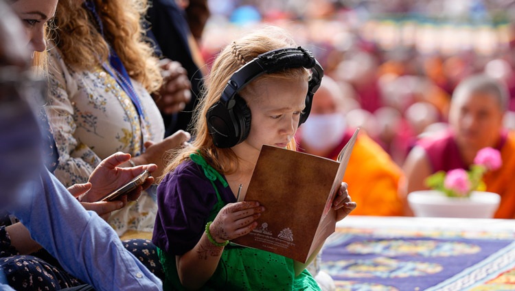A young girl listening to a live interpretation and following the text "Thirty-seven Practices of All Bodhisattvas" on the first day of teachings at the Shewatsel Teaching Area in Leh, Ladakh UT, India on July 21, 2023. Photo by Ven Zamling Norbu A young girl listening to a live interpretation and following the text "Thirty-seven Practices of All Bodhisattvas" on the first day of teachings at the Shewatsel Teaching Area in Leh, Ladakh UT, India on July 21, 2023. Photo by Ven Zamling Norbu